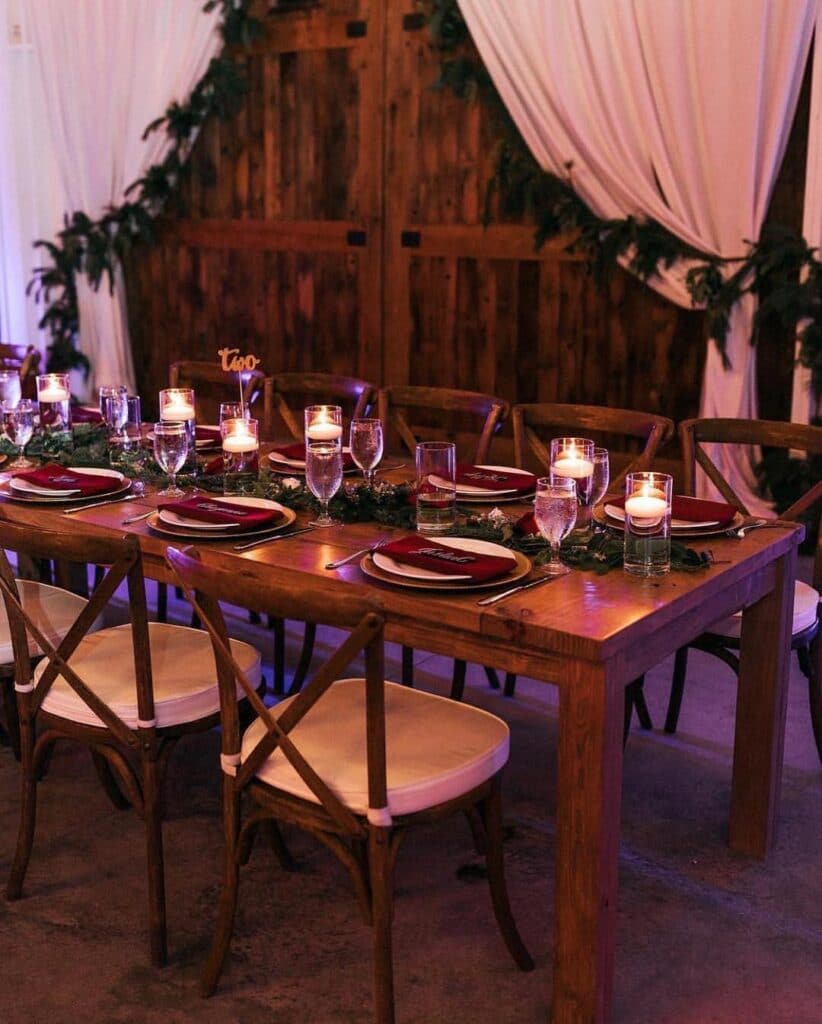 wood table and chairs set up for dinner with variety of candles and white curtains in background